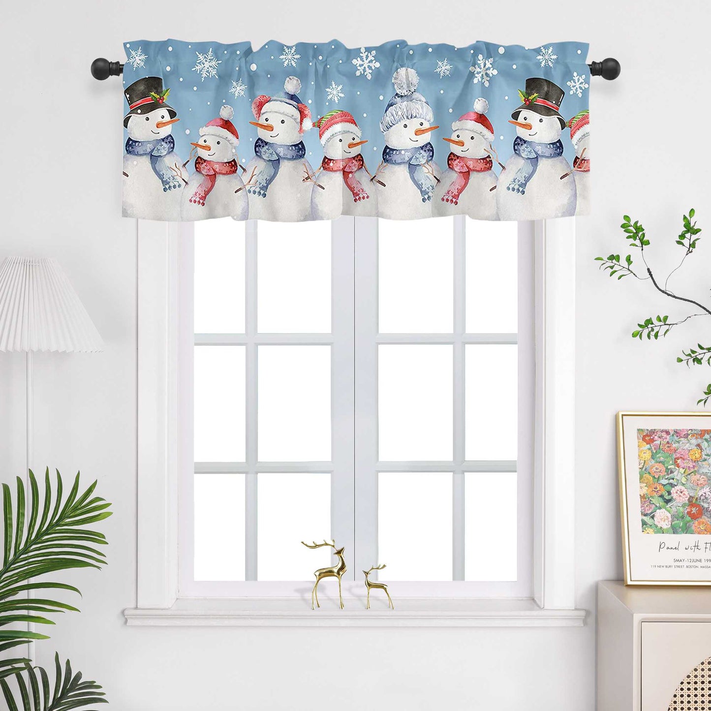 Die blaue Weihnachts-Scheibengardine mit Schneemann-Motiven bringt eine fröhliche und winterliche Atmosphäre in den Raum. Die Schneemänner und kleinen Schneeflocken sind mit pragmatischer Drucktechnik auf den Stoff aufgebracht, was ihnen klare Konturen und eine lebendige Darstellung verleiht. Diese Lichtschutzgardine hängt vor einem weißen Fenster und sorgt für eine gemütliche Weihnachtsstimmung. Die weiße Wand und grünen Pflanzen im Raum ergänzen das Design und bringen die festlichen Elemente perfekt zur G