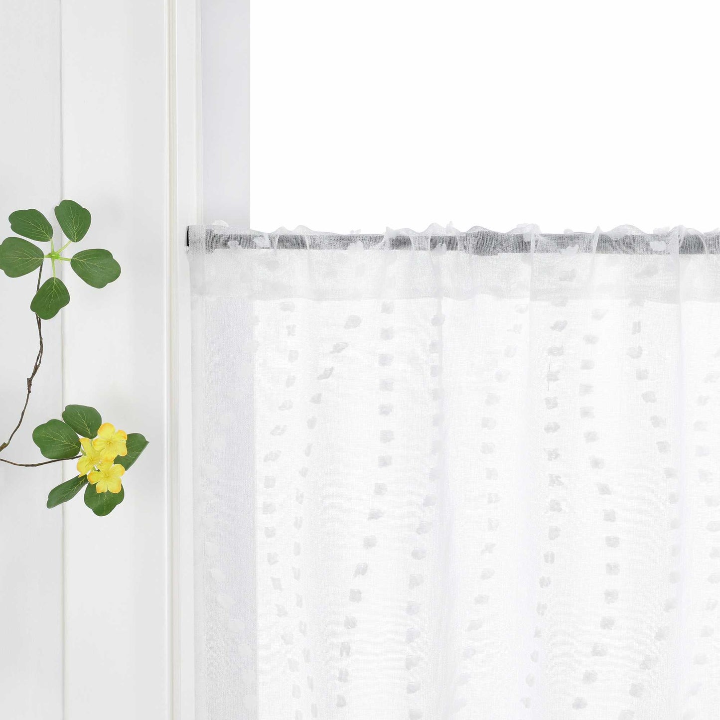 Die weiße Gardine mit dem 3D-Punktemuster hängt an einem Fenster, wobei die Aufhängung über die Schlaufen am Vorhangstab sichtbar ist. Das punktuelle Design der Gardine kommt klar zur Geltung und fügt dem Raum eine elegante Textur hinzu. Grüne Pflanzen am Fenster ergänzen das harmonische Gesamtbild und bringen Frische ins Zimmer.