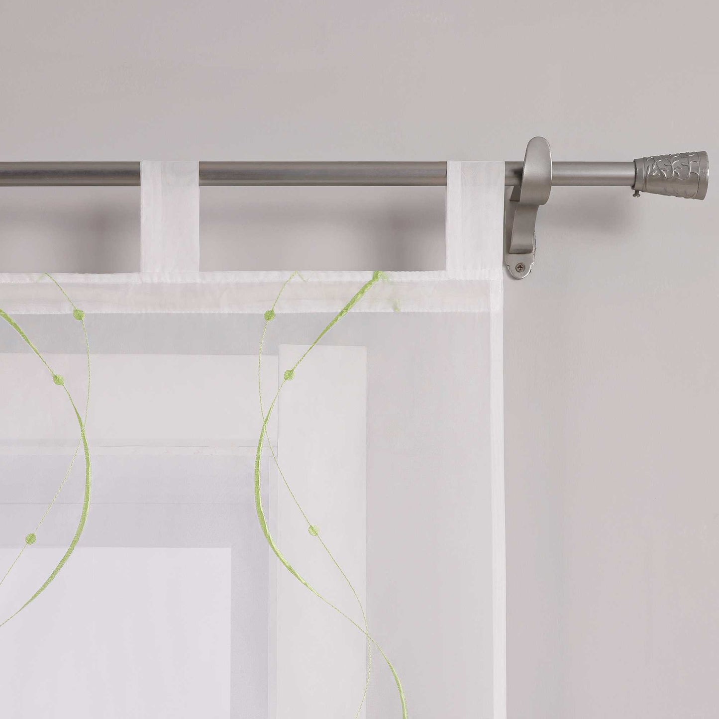 Das Bild zeigt die Details der Gardinenschlaufen. Die Gardine ist mit feinen grünen Naehten in Wellenform und kleinen Punkten am Ende verziert. Sie haengt mithilfe gleichmaessiger weisser Schlaufen an einer Metallstange. Die Verarbeitung an den Naehten ist sauber, das Material wirkt hochwertig.