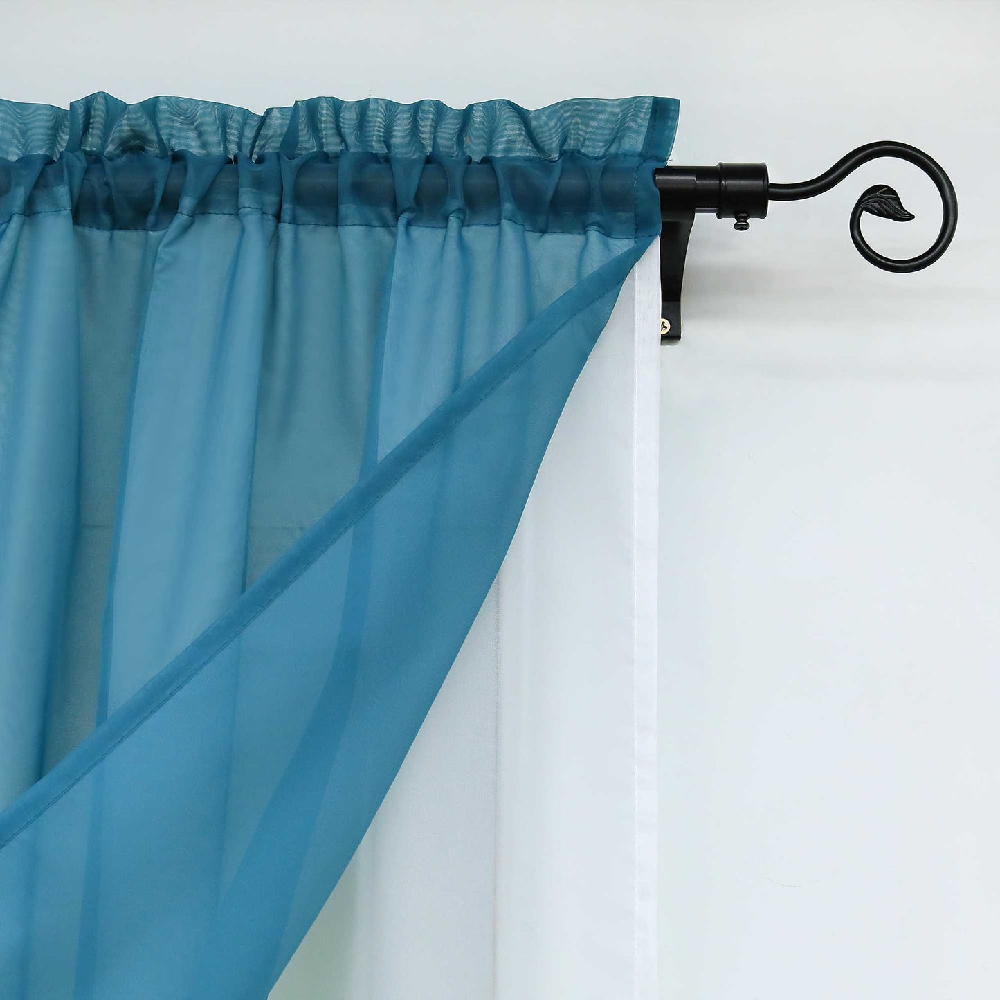 Nahaufnahme der blauen halbtransparenten Gardinen. Der Saum des oberen Teils der Gardinen sorgt für eine gleichmäßige Faltung, während die Gardinen an einer eleganten schwarzen Gardinenstange befestigt sind.