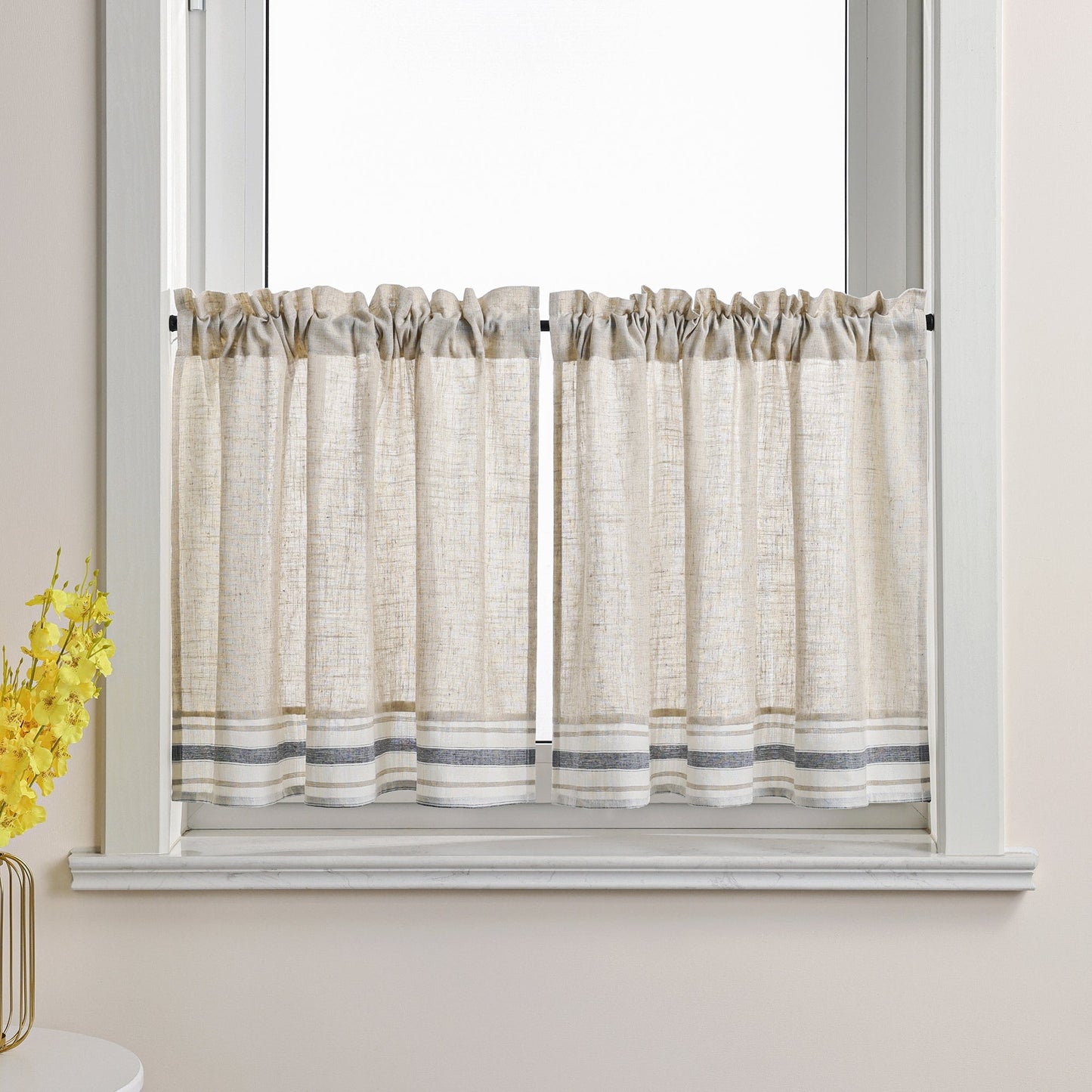 Dies ist eine Gardine im Landhausstil, die am Fenster angebracht ist. Der Hauptstoff ist cremeweiß mit einer Leinenstruktur. Der untere Rand ist mit grauen und weißen Streifen verziert. Diese Scheibengardinen im Landhausstil verleihen Ihrem Raum ein natürliches und schlichtes Ambiente. Sie passen gut zu verschiedenen Einrichtungsstilen wie skandinavischem oder japanischem Design und sorgen für sanftes Licht sowie eine warme, einladende Atmosphäre.