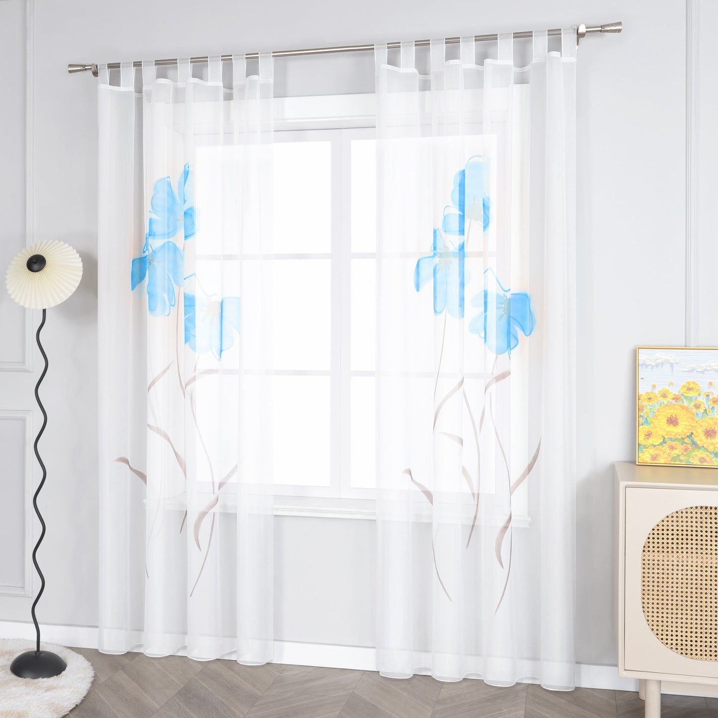 Das Bild zeigt einen weißen Vorhang mit blauen Blumenmustern und braunen Zweigen. Auf der linken Seite des Vorhangs steht eine Stehlampe, und auf der rechten Seite befindet sich ein kleiner Schrank, auf dem ein Gemälde steht.