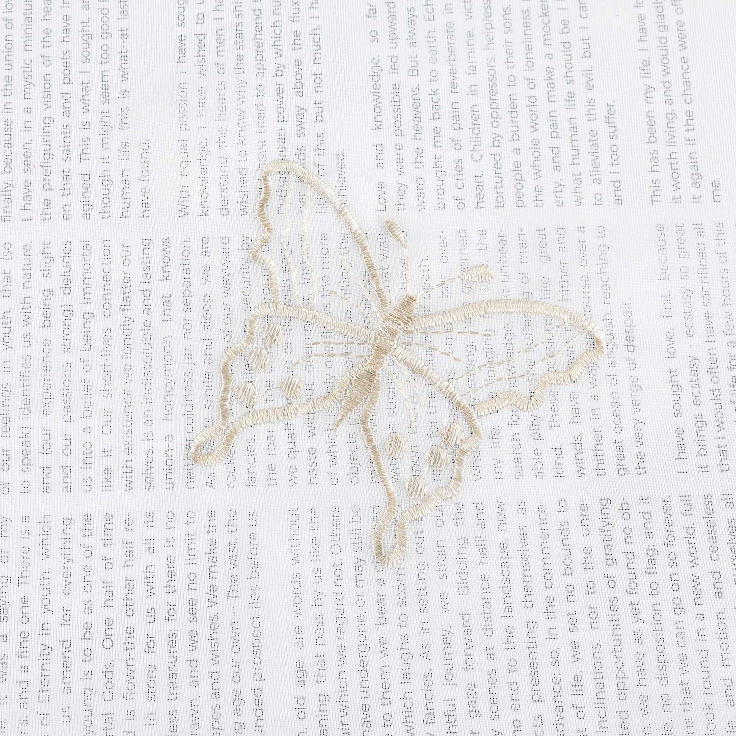 Nahaufnahme einer beigen Schmetterlingsstickerei, die auf einem transparenten weißen Stoff flach ausgebreitet liegt. Die beigen Schmetterlinge sind sorgfältig in das Gewebe eingearbeitet.