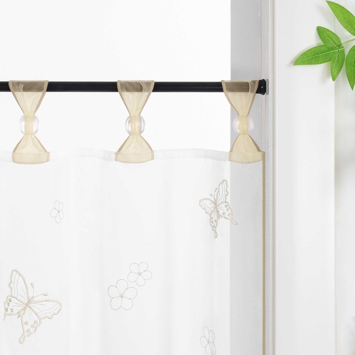Nahaufnahme der beige schlaufen mit transparenten Perlen, der Vorhang hängt an einer Stange und zeigt Schmetterlingsmuster, daneben sind Blumen als Dekoration.