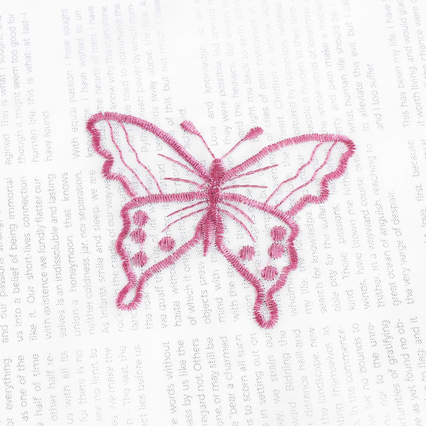 Nahaufnahme einer lila Schmetterlingsstickerei, die auf einem transparenten weißen Stoff flach ausgebreitet liegt. Die lila Schmetterlinge sind sorgfältig in das Gewebe eingearbeitet.