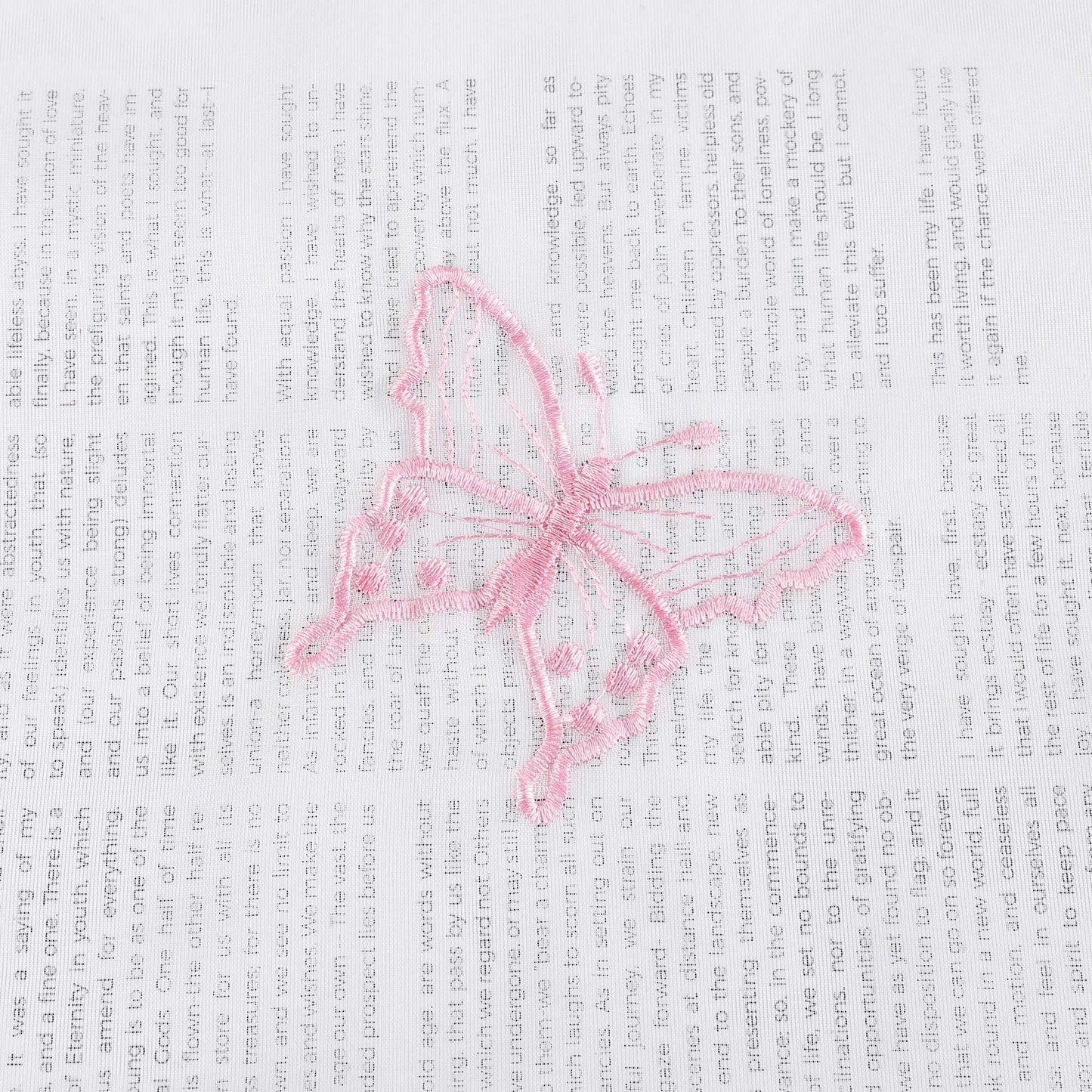 Nahaufnahme einer rosa Schmetterlingsstickerei, die auf einem transparenten weißen Stoff flach ausgebreitet liegt. Die rosa Schmetterlinge sind sorgfältig in das Gewebe eingearbeitet.