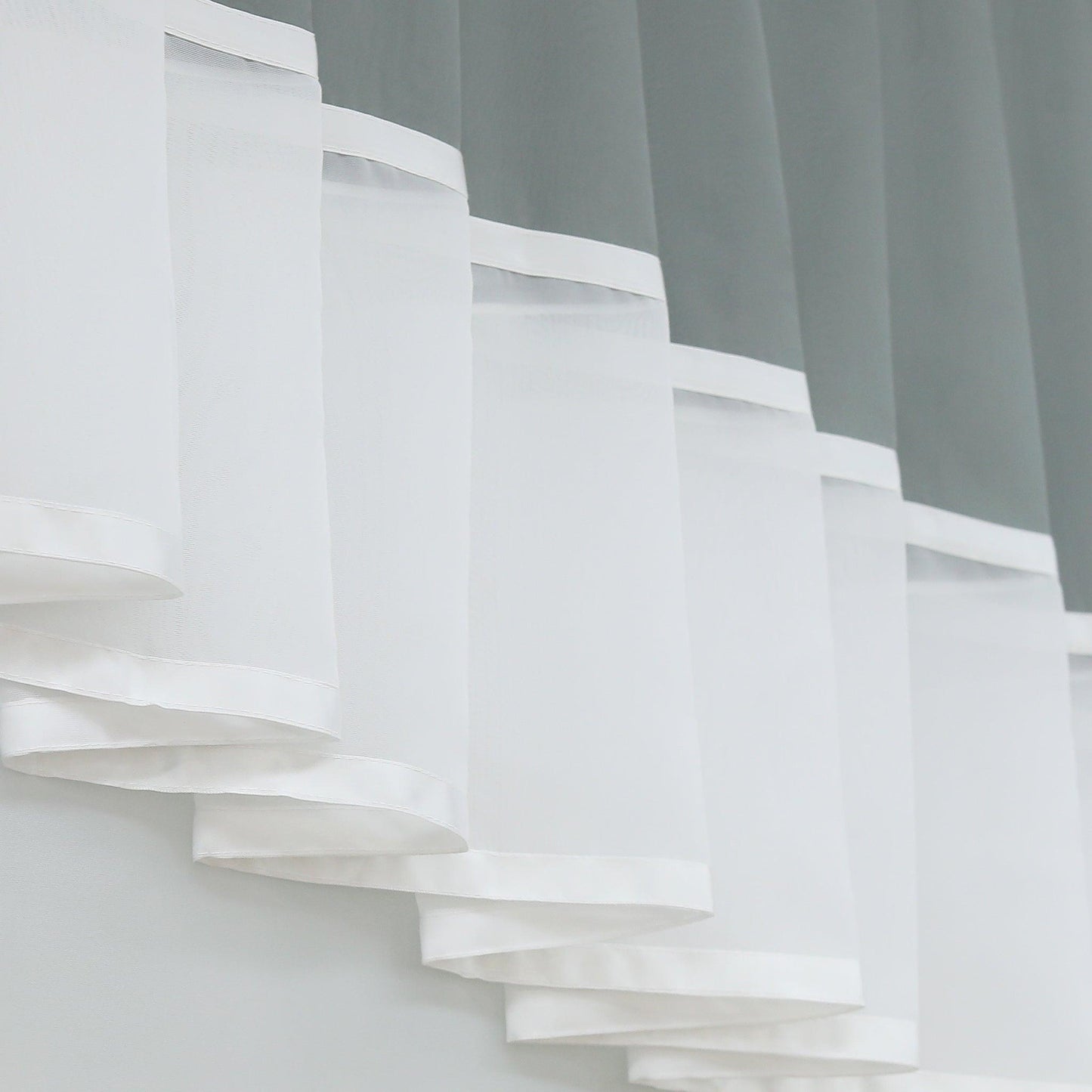 Dies ist ein Detailbild des weißen, transparenten Teils des Vorhangs. Der Stoff ist leicht und weist eine saubere Kantenborte auf. Die Falten sind schichtweise angeordnet, was dem Vorhang eine schöne, dekorative Struktur und eine harmonische Tiefe verleiht.