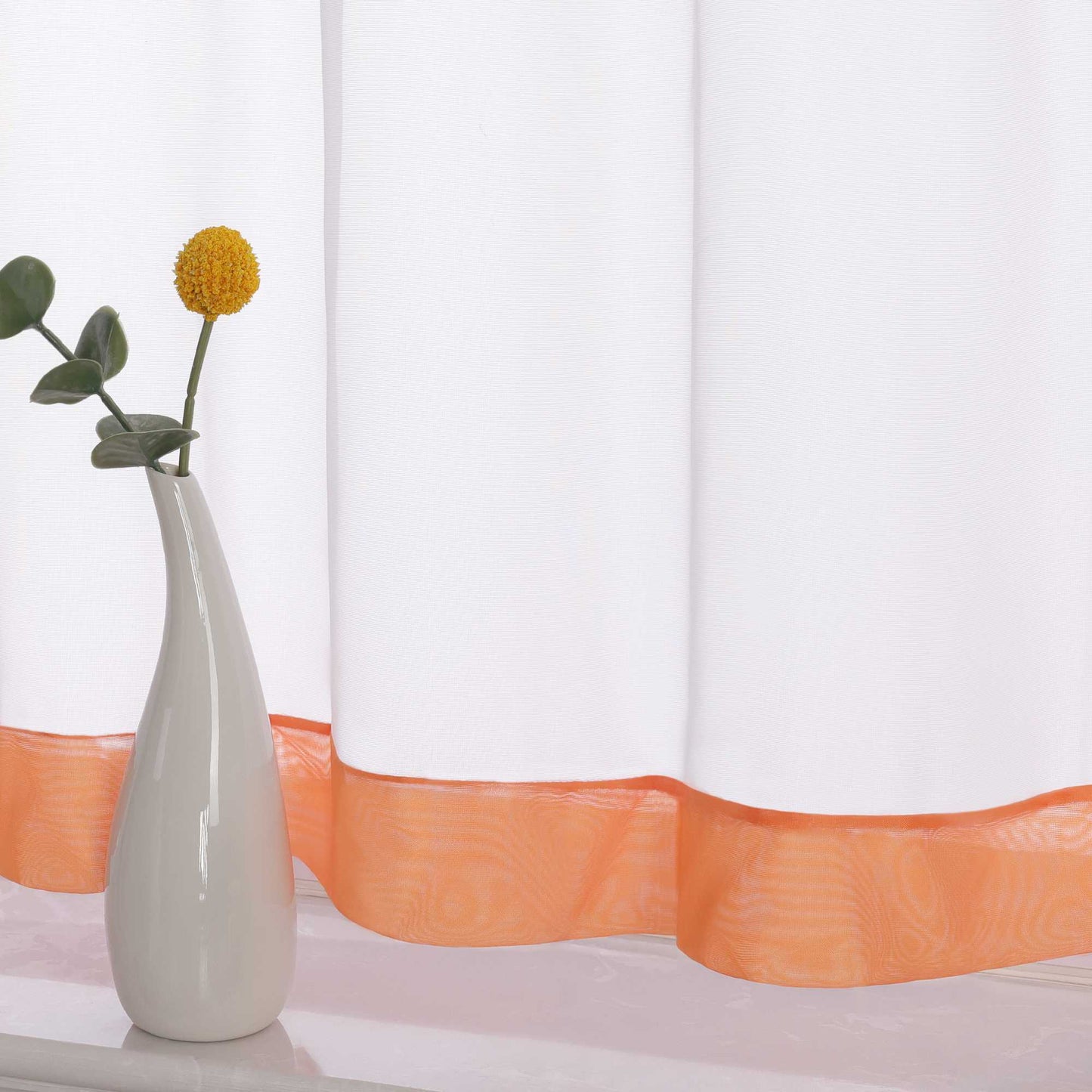 Die Unterkante des Vorhangs wird im Detail gezeigt, mit einem orange Dekorband als stilvollem Akzent. Ein Vase im Vordergrund ergänzt die Szene und fügt dem Raum eine harmonische, dekorative Note hinzu, die den eleganten Look des Vorhangs unterstreicht.