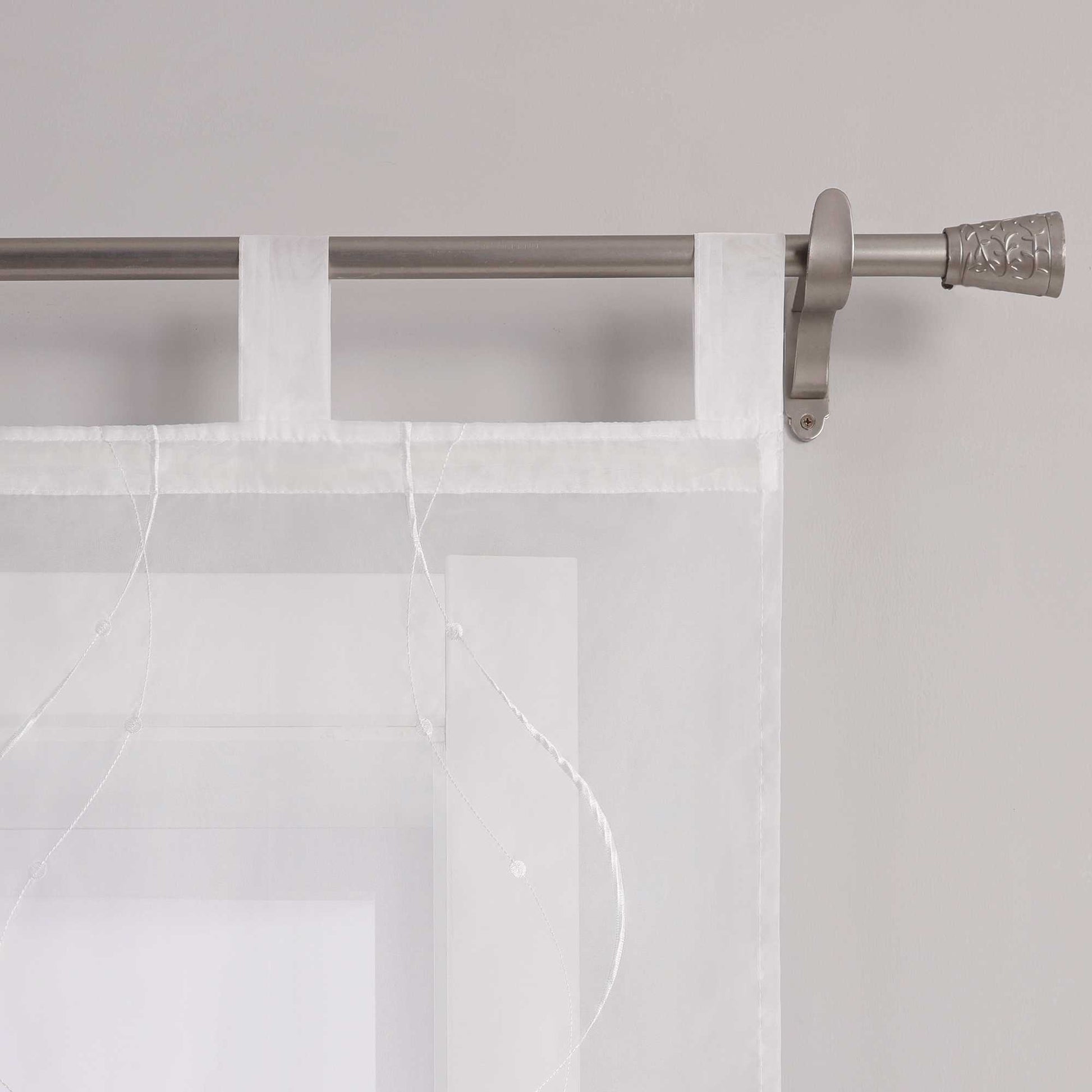 Das Bild zeigt die Details der Schlaufen einer weissen Gardine. Die Gardine ist mit feiner weisser Naht in Wellenform und kleinen Punkten am Ende verziert. Sie haengt mithilfe gleichmaessiger weisser Schlaufen an einer Metallstange. Die Naehte sind sauber verarbeitet und das Material wirkt hochwertig.