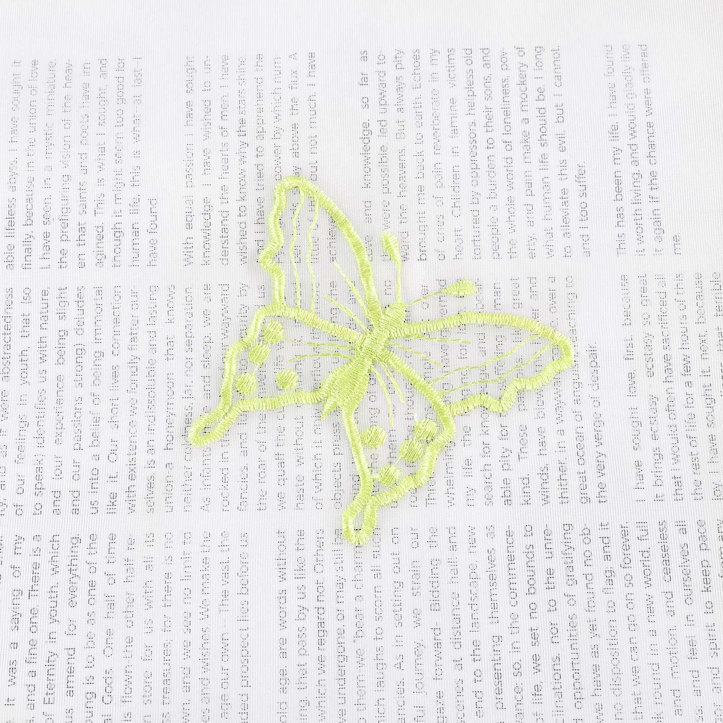 Nahaufnahme einer grünen Schmetterlingsstickerei, die auf einem transparenten weißen Stoff flach ausgebreitet liegt. Die grünen Schmetterlinge sind sorgfältig in das Gewebe eingearbeitet.