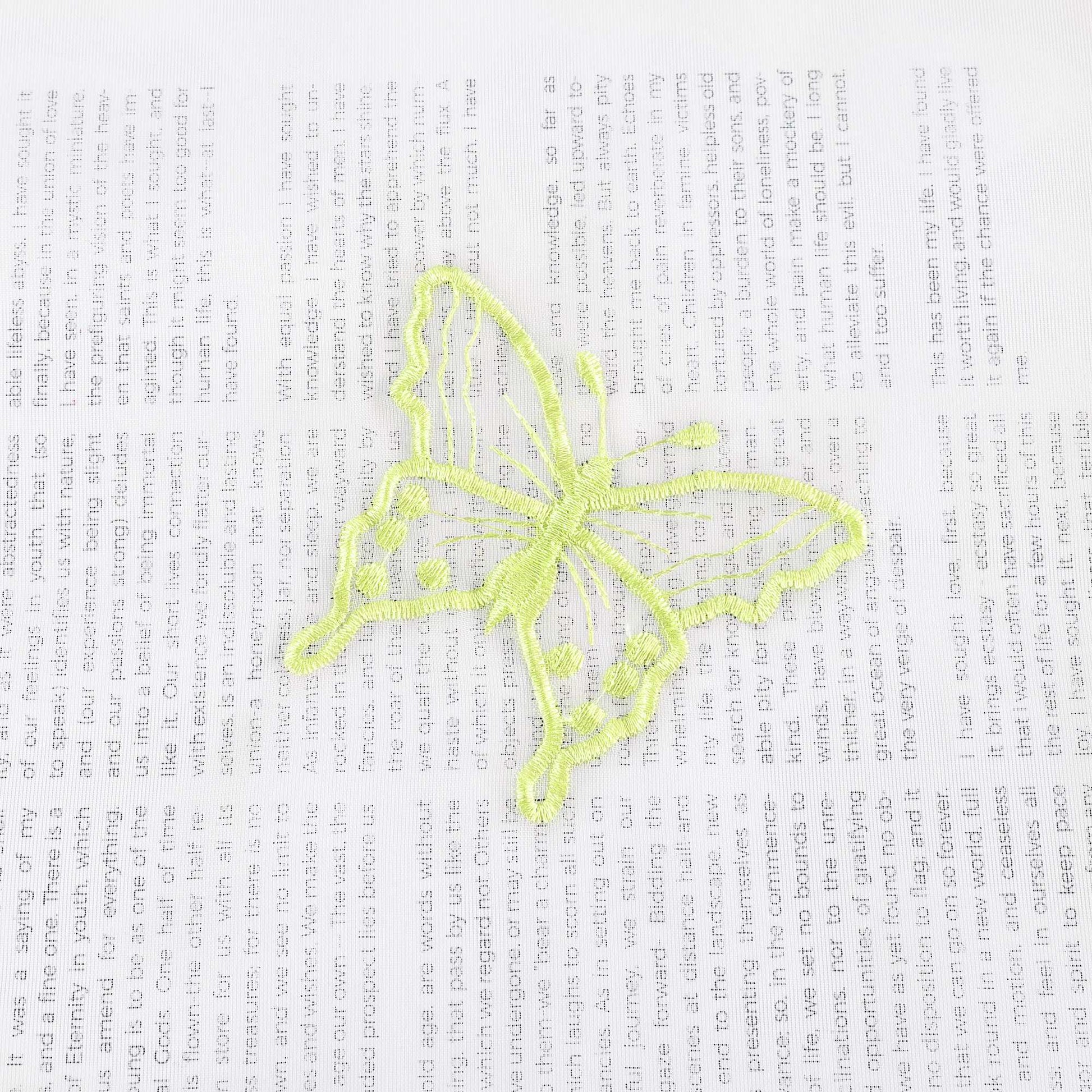 Nahaufnahme einer grünen Schmetterlingsstickerei, die auf einem transparenten weißen Stoff flach ausgebreitet liegt. Die grünen Schmetterlinge sind sorgfältig in das Gewebe eingearbeitet.