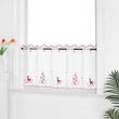 Die transparente Kurzgardine hängt festlich vor einem weißen Fenster. Die Gardine ist mit roten Nähten verziert und zeigt handgestickte Motive von Schneeflocken, Rentieren und einem Weihnachtsbaum, die eine weihnachtliche Atmosphäre schaffen. Die weiße Wand im Hintergrund sorgt für eine helle und neutrale Kulisse, während die pflanzlichen Dekorationen rund um das Fenster eine natürliche und gemütliche Stimmung verleihen. Der transparente Stoff lässt viel Tageslicht herein und sorgt für eine subtile, aber fe