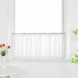 Die weiße, transparente Scheibengardine hängt vor einem Fenster und zeigt ein elegantes 3D-Punktemuster auf der Oberfläche. Der Fensterbereich wird durch grüne Pflanzen dekoriert, die dem Raum eine frische und lebendige Atmosphäre verleihen.