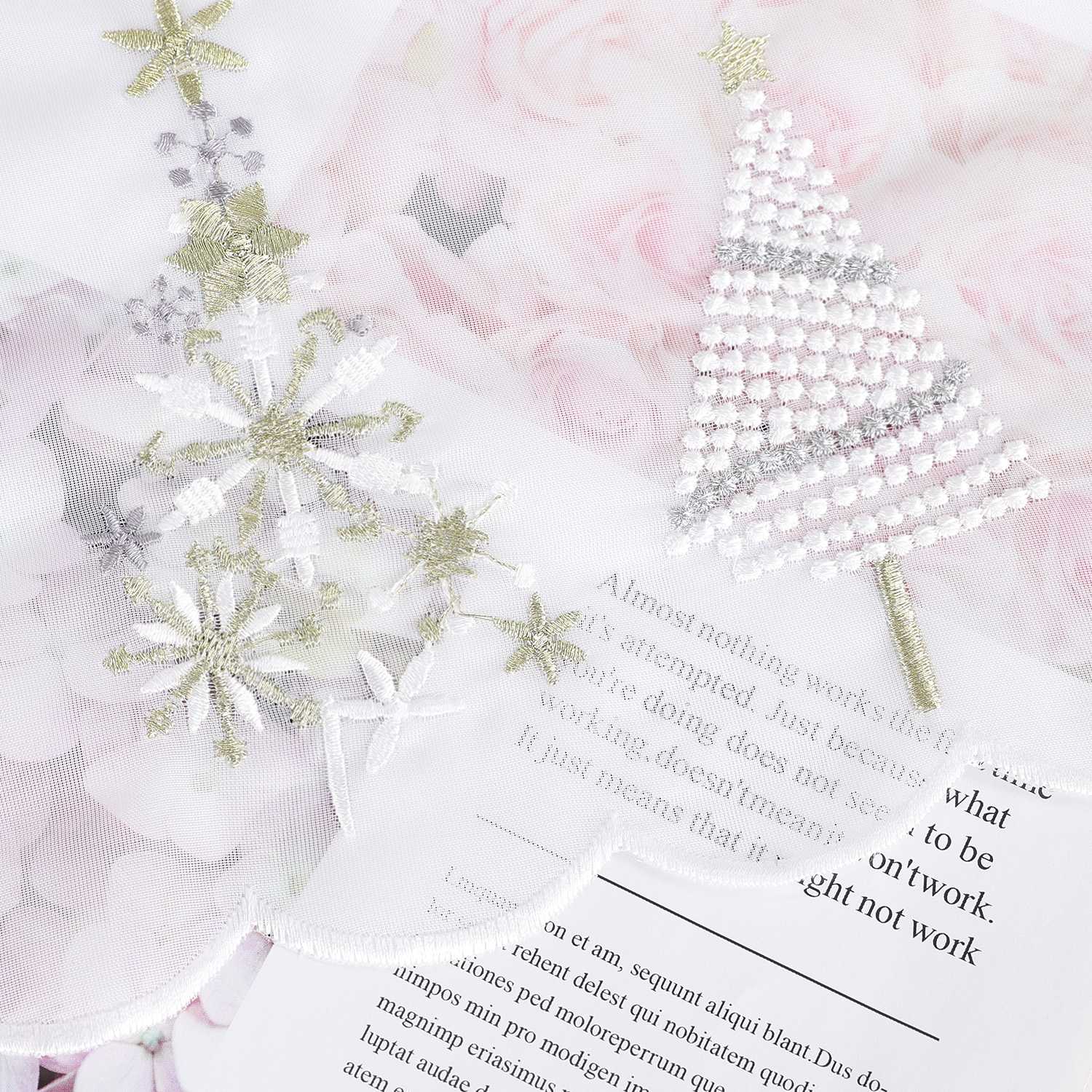 Auf dem weißen Stoff sind festliche Tannenbäume aufgestickt. Die feinen Details der Bäume – wie die geschwungenen Zweige, goldene Akzente und filigrane Linien – verleihen dem Muster eine elegante und weihnachtliche Ausstrahlung.