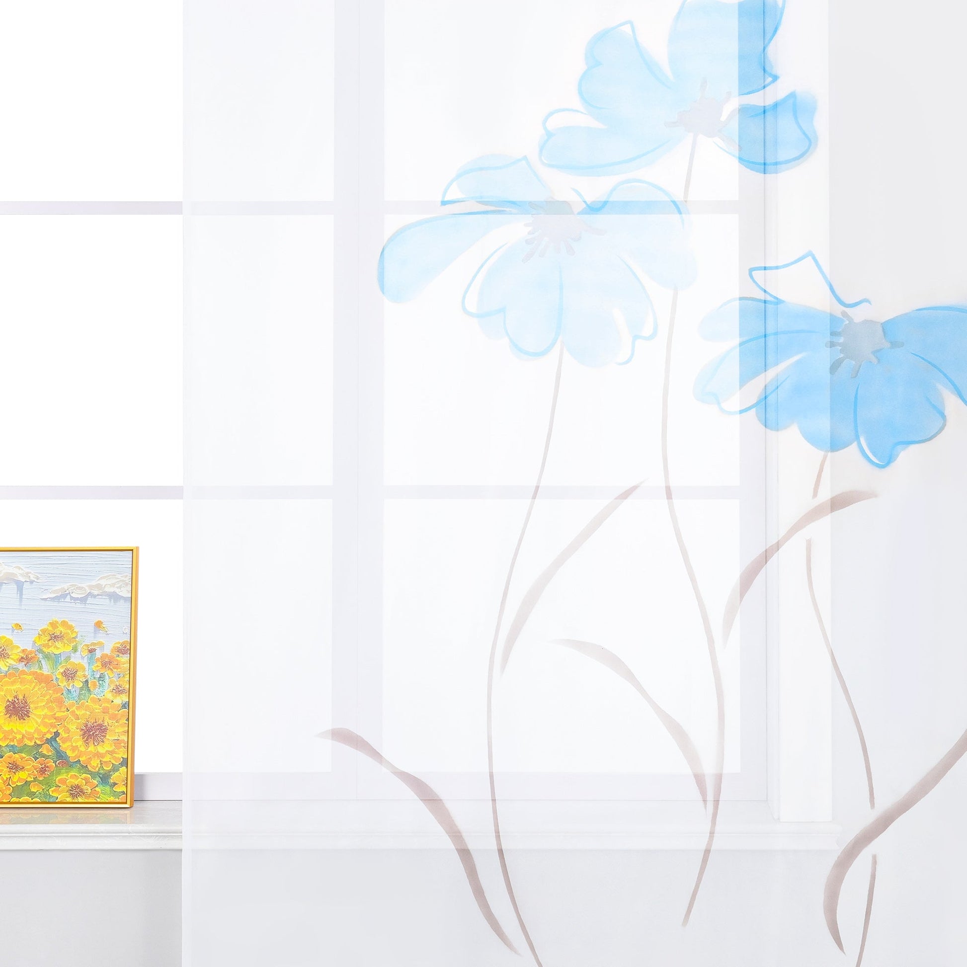 Das Bild zeigt einen weißen Vorhang mit blauen Blumenmustern. Das Design lässt die Blumen wie in der Luft schwebend erscheinen. Auf der Fensterbank steht ein dekoratives Bild, das gelbe Blumen darstellt. Insgesamt vermittelt die Szene einen frischen und hellen Eindruck.