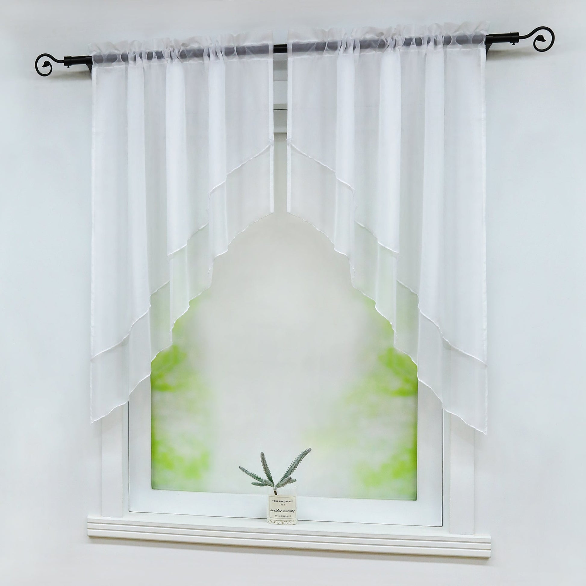 Seitliche Ansicht eines Fensters mit weißen, halbtransparenten Vorhängen, die symmetrisch diagonal geschnitten sind. Eine kleine grüne Pflanze steht dekorativ auf der Fensterbank vor einem weichen, grünen Hintergrund.