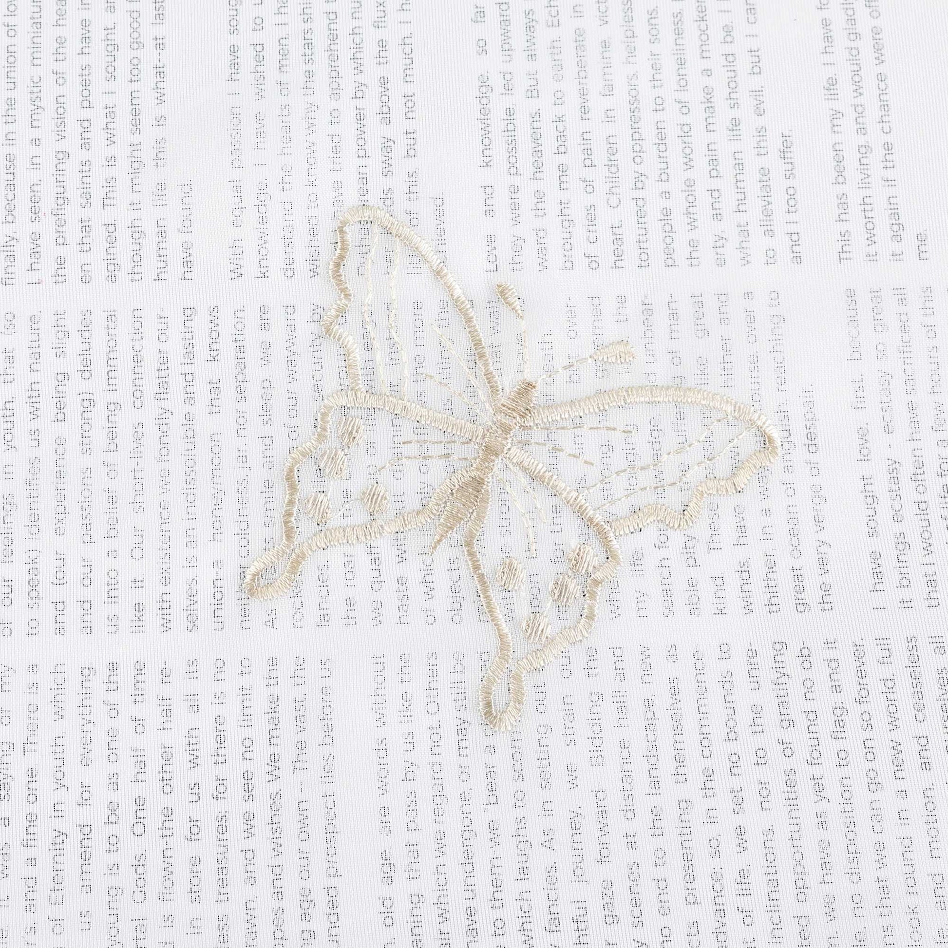 Nahaufnahme einer beigen Schmetterlingsstickerei, die auf einem transparenten weißen Stoff flach ausgebreitet liegt. Die beigen Schmetterlinge sind sorgfältig in das Gewebe eingearbeitet.