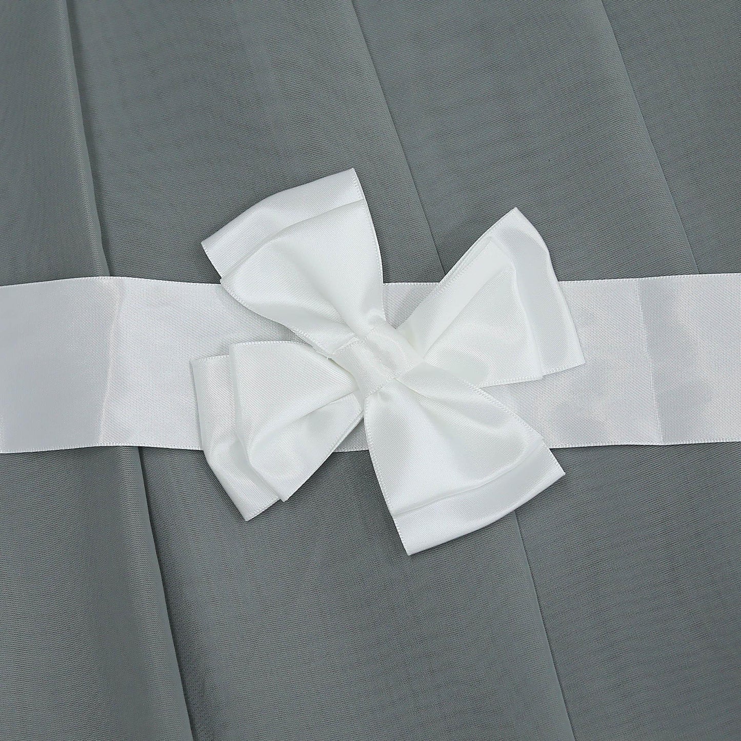 Dies ist ein Detailbild des Vorhangs. Auf dem grauen Stoff befindet sich ein weißes Webband, an dem eine weiße Schleife befestigt ist. Die Schleife ist fein gearbeitet und verleiht dem Vorhang eine elegante und dekorative Note.