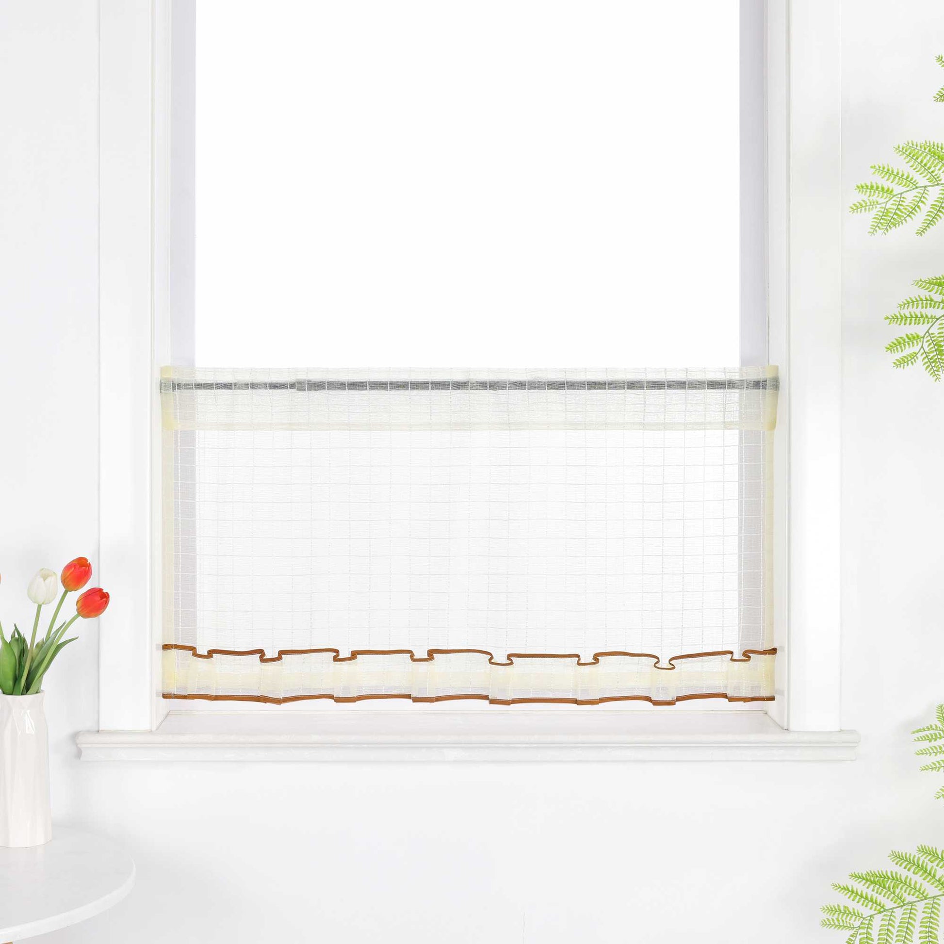 Gelber, transparenter Kurzvorhang hängt vor dem Fenster. Die Oberfläche zeigt ein feines Karomuster, unten verläuft ein dekoratives Band in Braun. Der obere Rand ist gerafft und bildet leichte Falten.