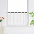 Weiße Scheibengardine hängt vor einem Fenster mit weißer Wand. Daneben sorgen rote Blumen, grüne Blätter und eine Vase für eine frische und dekorative Note.