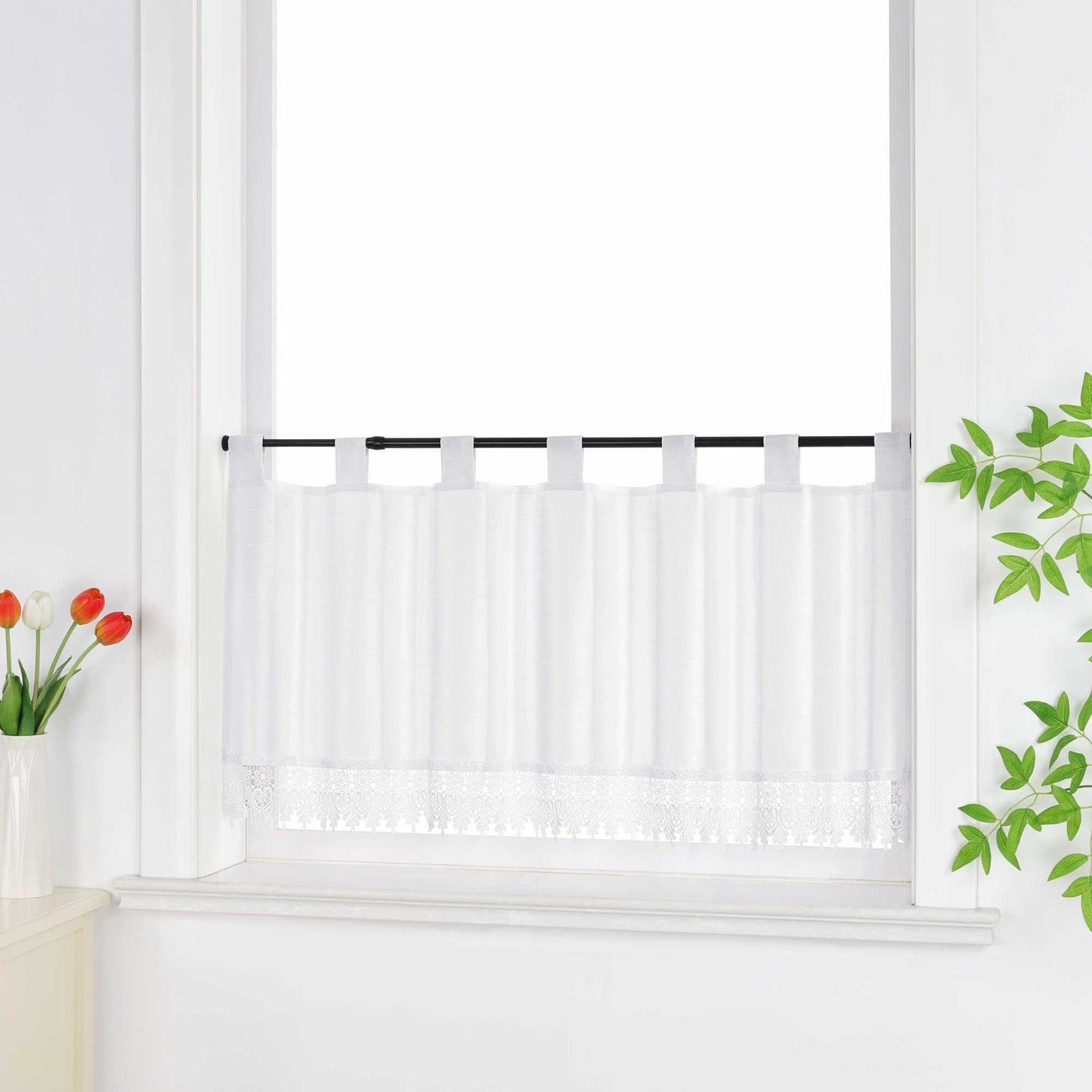 Seitlich aufgenommene Scheibengardine weiss vor dem Fenster, dekoriert mit grünen Blättern und Blüten.