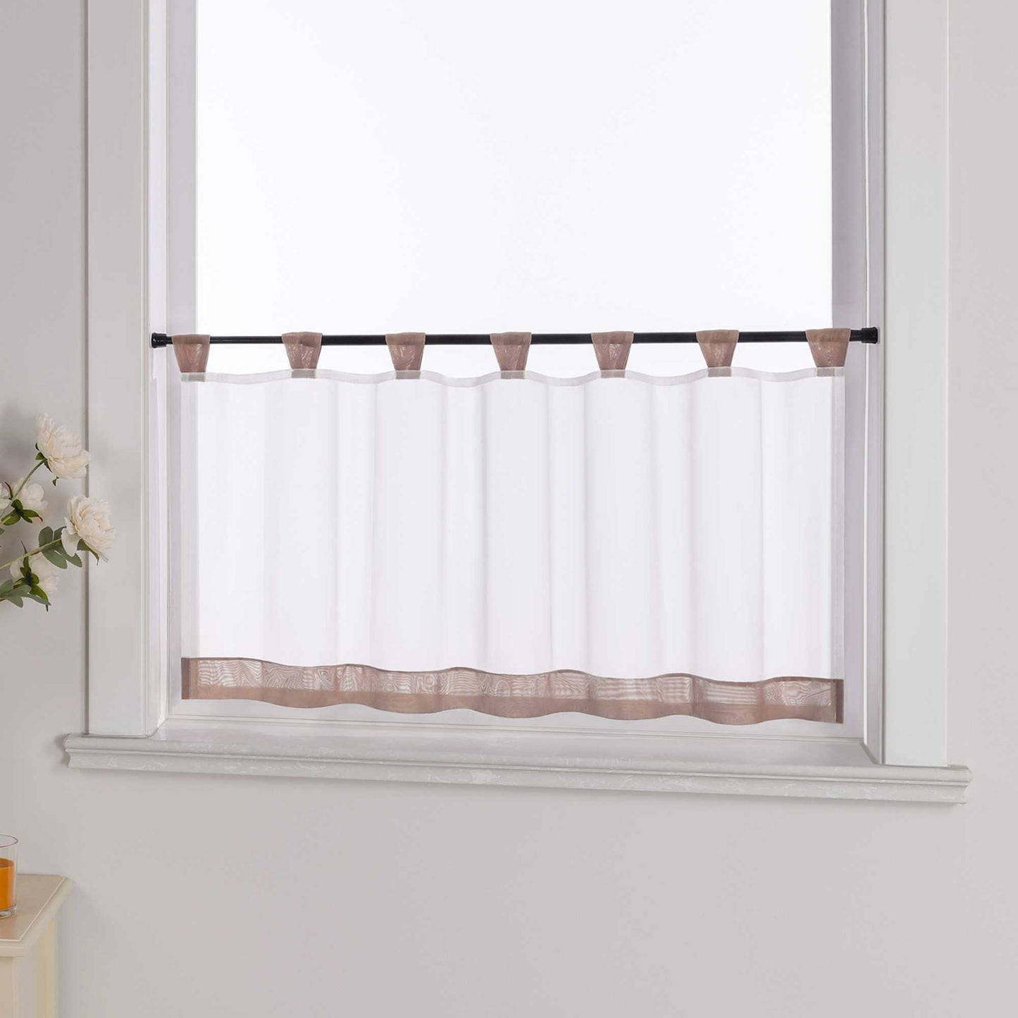 Die braune Scheibengardine hängt vor einem Fenster, während die weiße Hintergrundwand im Hintergrund sichtbar bleibt. Der transparente Vorhang lässt das Licht durch, während er von blumigen Dekorationen an der Seite sanft ergänzt wird, was dem Raum eine leichte und frische Atmosphäre verleiht.