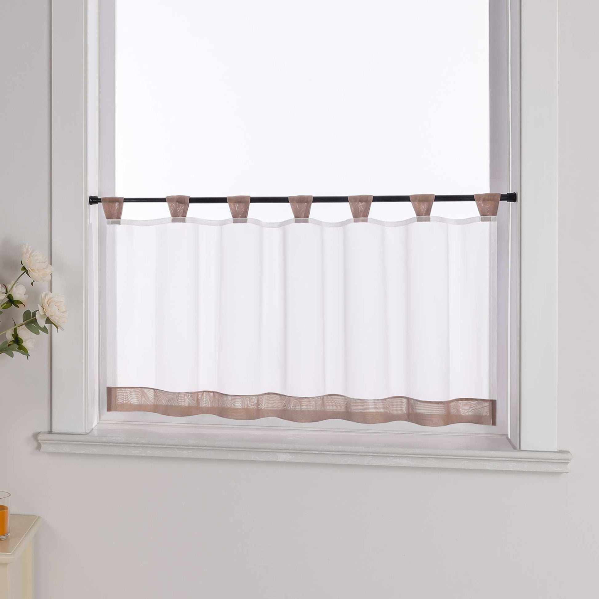 Die braune Scheibengardine hängt vor einem Fenster, während die weiße Hintergrundwand im Hintergrund sichtbar bleibt. Der transparente Vorhang lässt das Licht durch, während er von blumigen Dekorationen an der Seite sanft ergänzt wird, was dem Raum eine leichte und frische Atmosphäre verleiht.