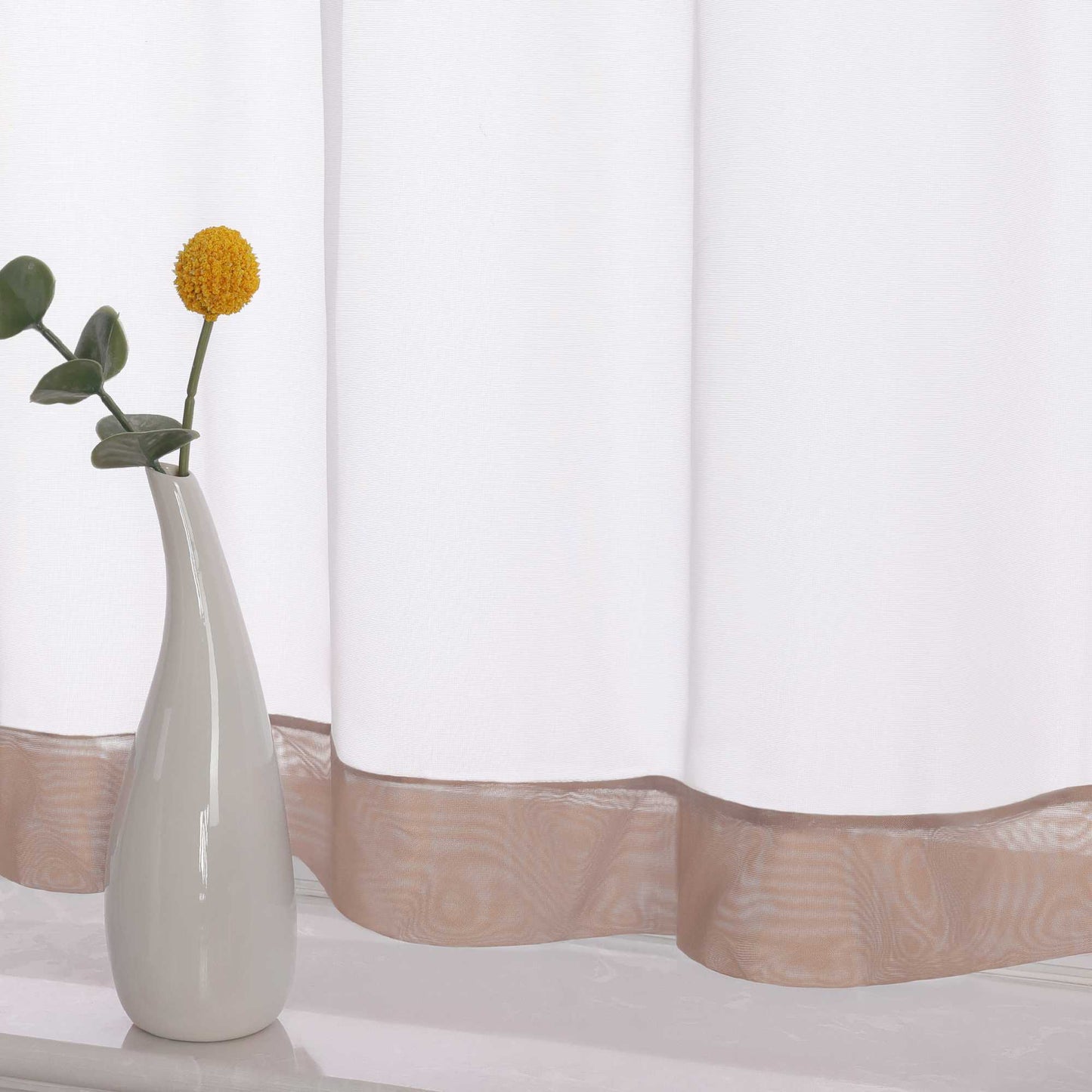 Die Unterkante des Vorhangs wird im Detail gezeigt, mit einem braunem Dekorband als stilvollem Akzent. Ein Vase im Vordergrund ergänzt die Szene und fügt dem Raum eine harmonische, dekorative Note hinzu, die den eleganten Look des Vorhangs unterstreicht.