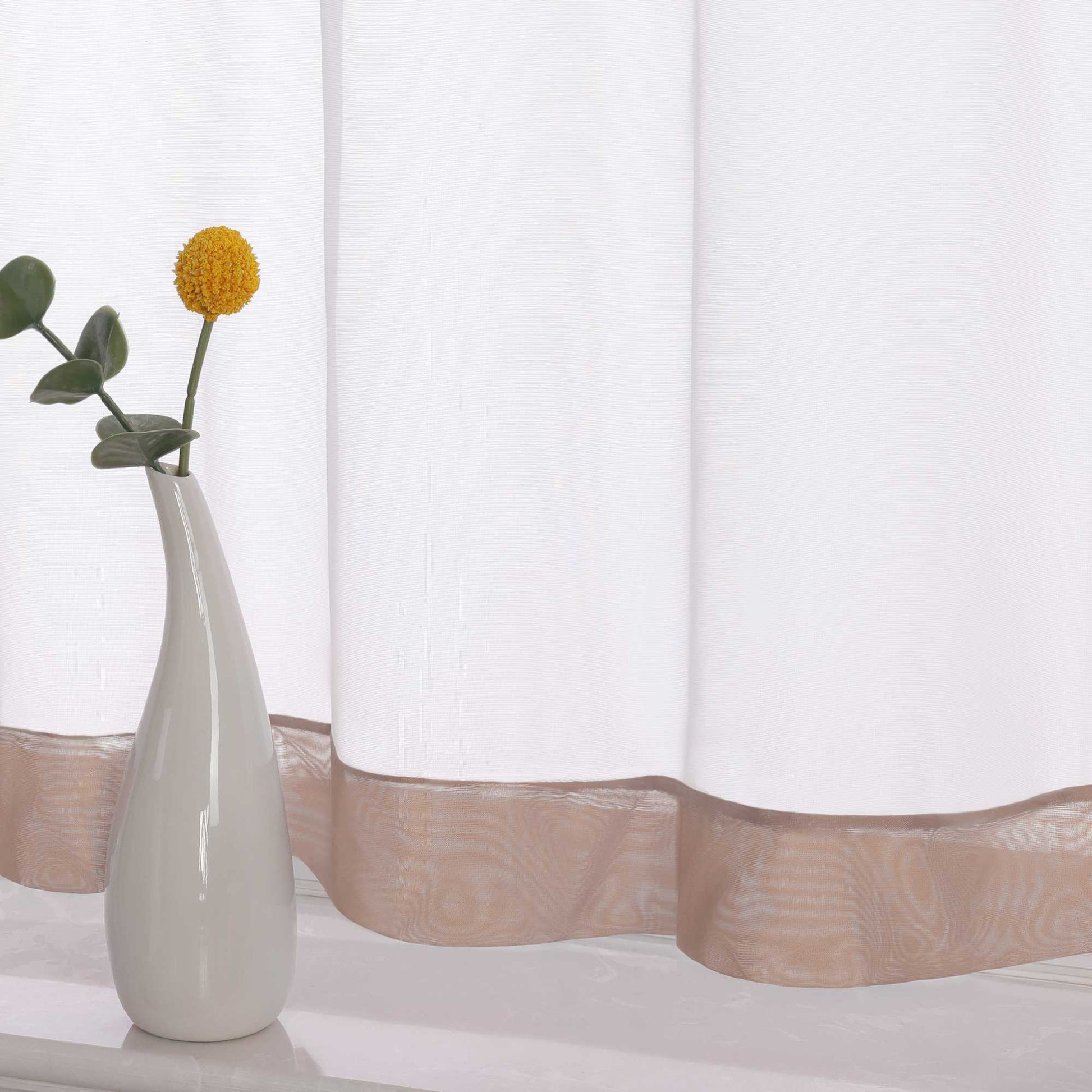 Die Unterkante des Vorhangs wird im Detail gezeigt, mit einem braunem Dekorband als stilvollem Akzent. Ein Vase im Vordergrund ergänzt die Szene und fügt dem Raum eine harmonische, dekorative Note hinzu, die den eleganten Look des Vorhangs unterstreicht.