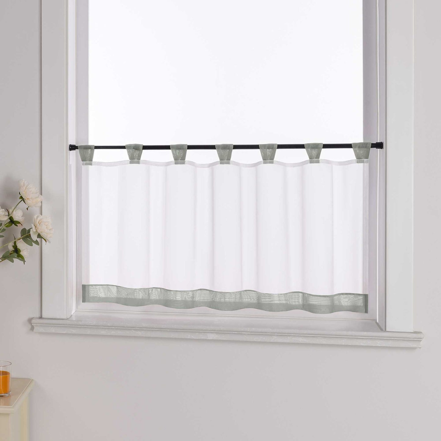 Der weiße Vorhang mit grauem Dekorband wird aus einem seitlichen Winkel fotografiert. Die weiße Wand im Hintergrund betont die Schlichtheit des Designs, während blumige Dekorationen an der Seite dem Raum eine zarte, natürliche Atmosphäre verleihen.