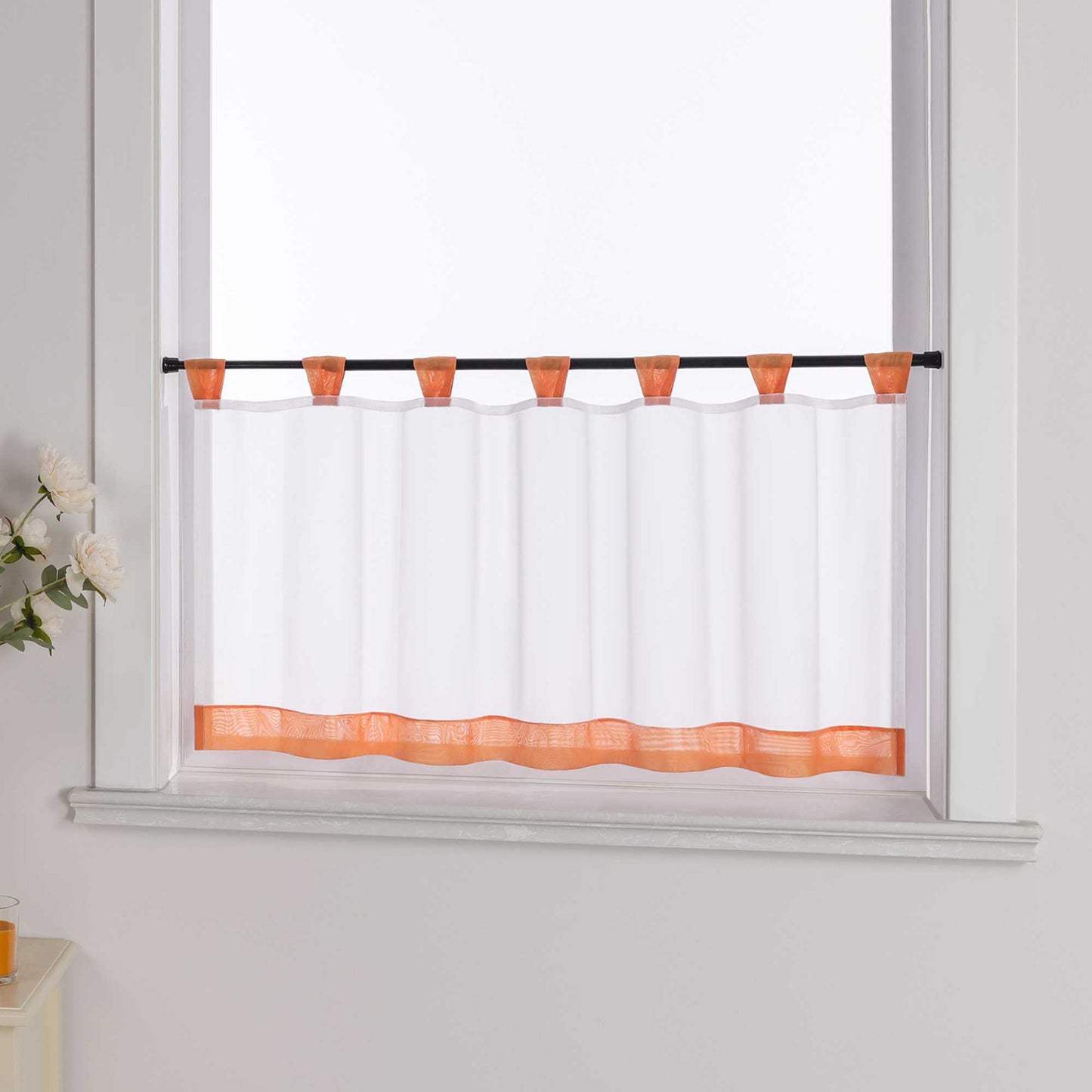 Der weiße Vorhang mit orange Dekorband wird aus einem seitlichen Winkel fotografiert. Die weiße Wand im Hintergrund betont die Schlichtheit des Designs, während blumige Dekorationen an der Seite dem Raum eine zarte, natürliche Atmosphäre verleihen.
